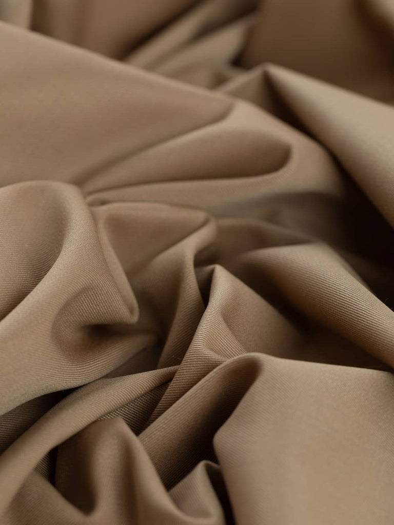 Angled twist shot of Golden Sand fabric, highlighting its smooth texture and warm, golden beige tone. The fabric’s fine twill weave offers durability and comfort, ideal for both casual and formal garment creations.