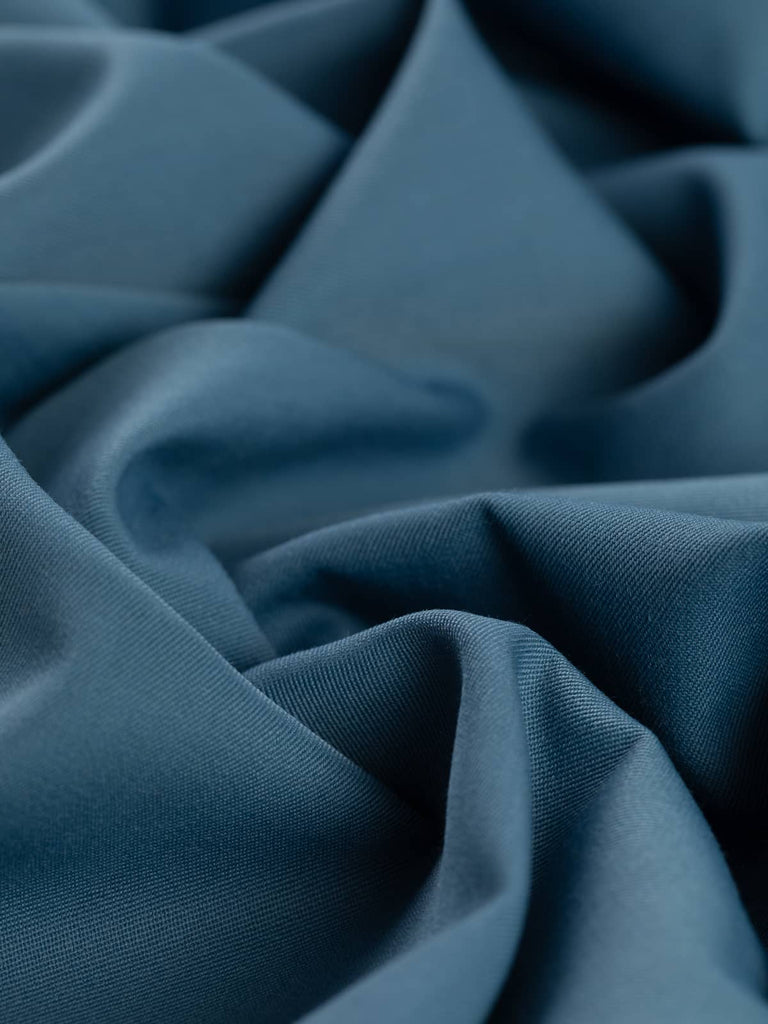 Angled twist shot of the Cool Sky wool-blend fabric, revealing soft folds and a fluid drape. The serene blue hue with grey notes is enhanced by the fine twill texture and subtle luster, reflecting its versatile, utility-to-formal potential.
