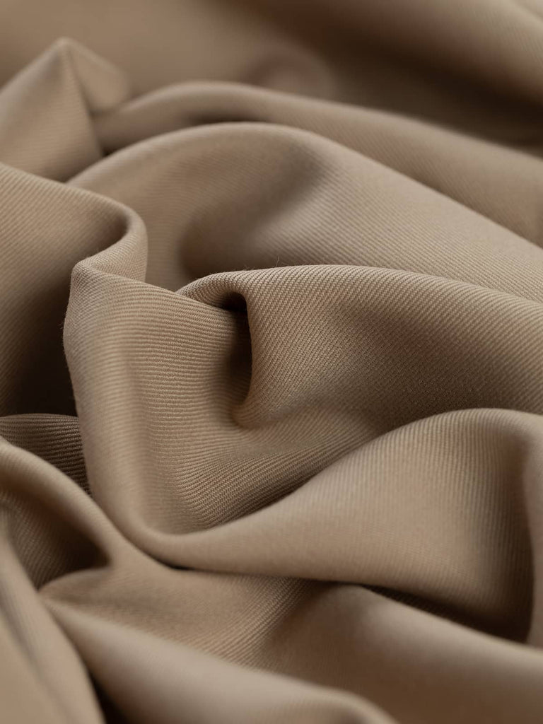 Angled twist shot of Latte Beige fabric, highlighting its silky-soft wool-poly blend and fluid drape. The understated beige tone enhances its versatility for both smart and casual pieces.