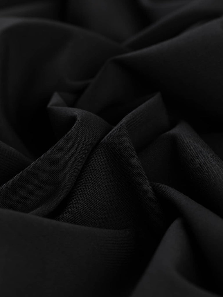 Angled twist shot of Coal Dust fabric, highlighting its fluid drape, soft wool-poly blend, and rich, even black hue. Perfect for elegant or utilitarian styles.
