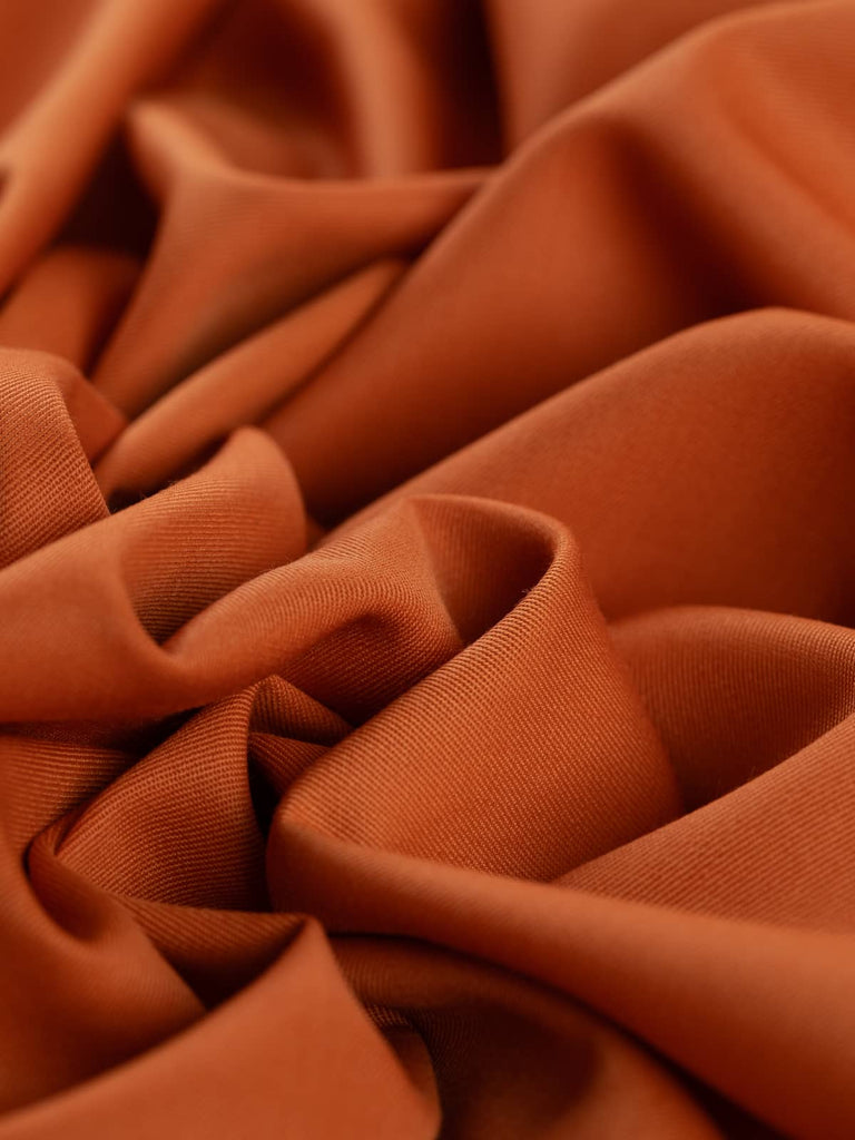 Angled twist shot of Rusty Orange fabric, highlighting its soft wool-poly blend, fluid drape, and mellow earthy hue. Perfect for distinctive vintage or autumn-inspired garments.