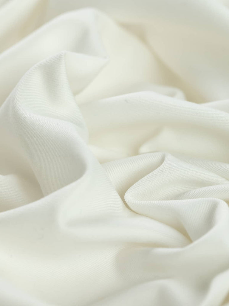 Angled twist shot showing the smooth, close twill texture of wool and polyester Pearl White fabric, highlighting its soft drape and subtle pearlescent glow.