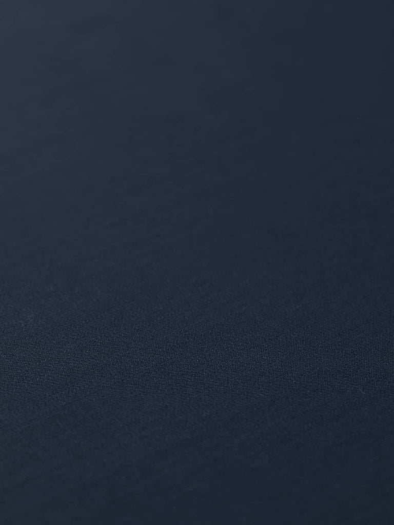 Angled flat lay of Peerless Navy fabric, displaying its even, deep navy tone and impeccable worsted-style finish. The fine wool and polyester blend offers a smooth, stable surface with an elegant, understated drape