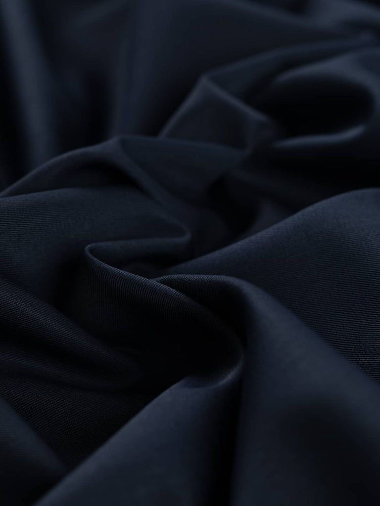 Close-up angled twist of Peerless Navy wool-blend fabric, showing its rich, all-over navy hue and soft yet durable handle. The fine weave catches subtle light, revealing its crease-resistant, smooth worsted texture.