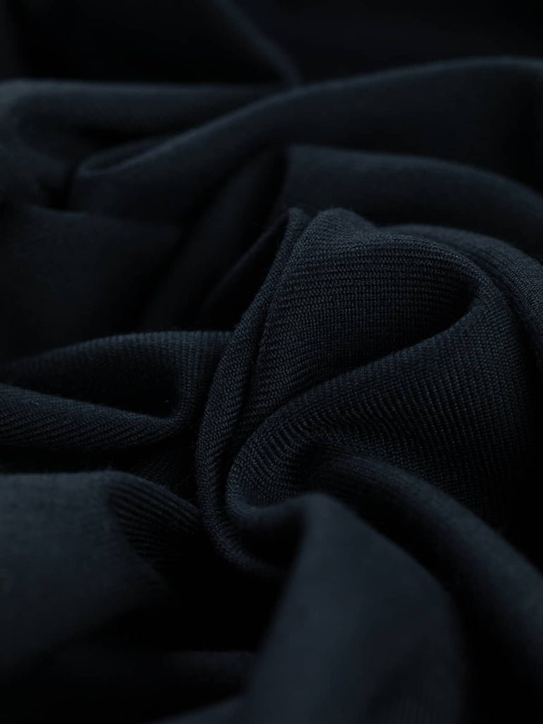 Close-up angled twist of Seriously Navy wool-blend serge, highlighting its deep navy hue, lightly brushed fine wool texture, and distinctive twill diagonal lines. The fabric shows durability with an elegant, structured drape.