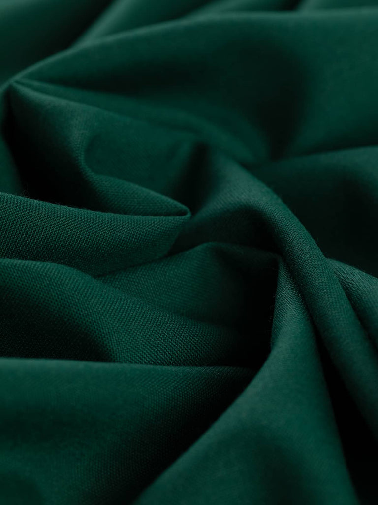 Close-up twist of Heritage Green worsted wool-blend, showing its solid racing green hue, fine worsted texture, and elegant structured drape with subtle sheen.