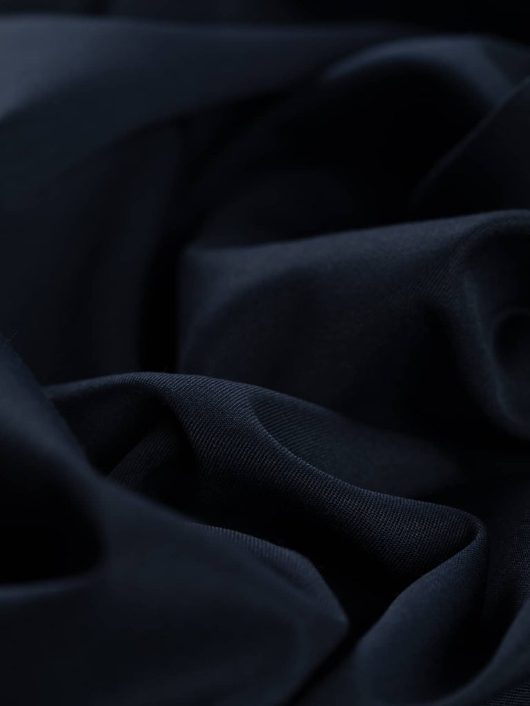 Close-up twist of Oxford Noir wool-blend fabric, showing even gabardine twill texture, soft drape, and refined navy-black hue ideal for tailored garments
