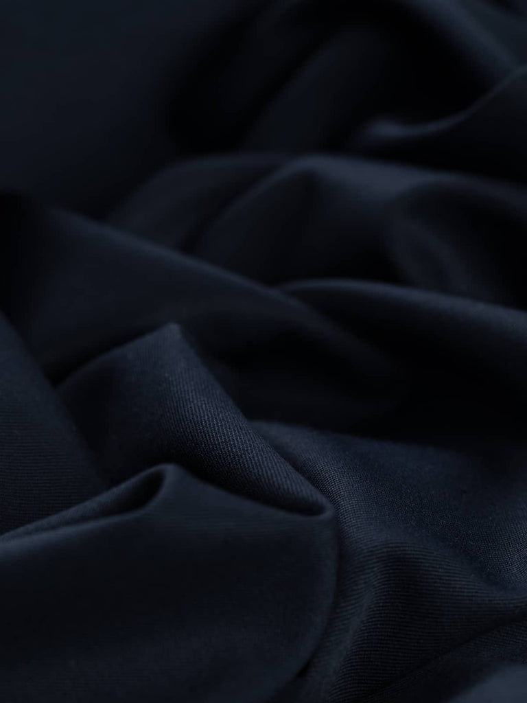 Close-up twist of Oxford Noir wool-blend fabric, showing even gabardine twill texture, soft drape, and refined navy-black hue ideal for tailored garments