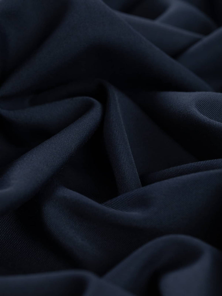 Close-up twist of Sapphire Smoke wool-blend fabric, showing its soft drape, moody navy-grey hue, and fine twill weave with elegant body