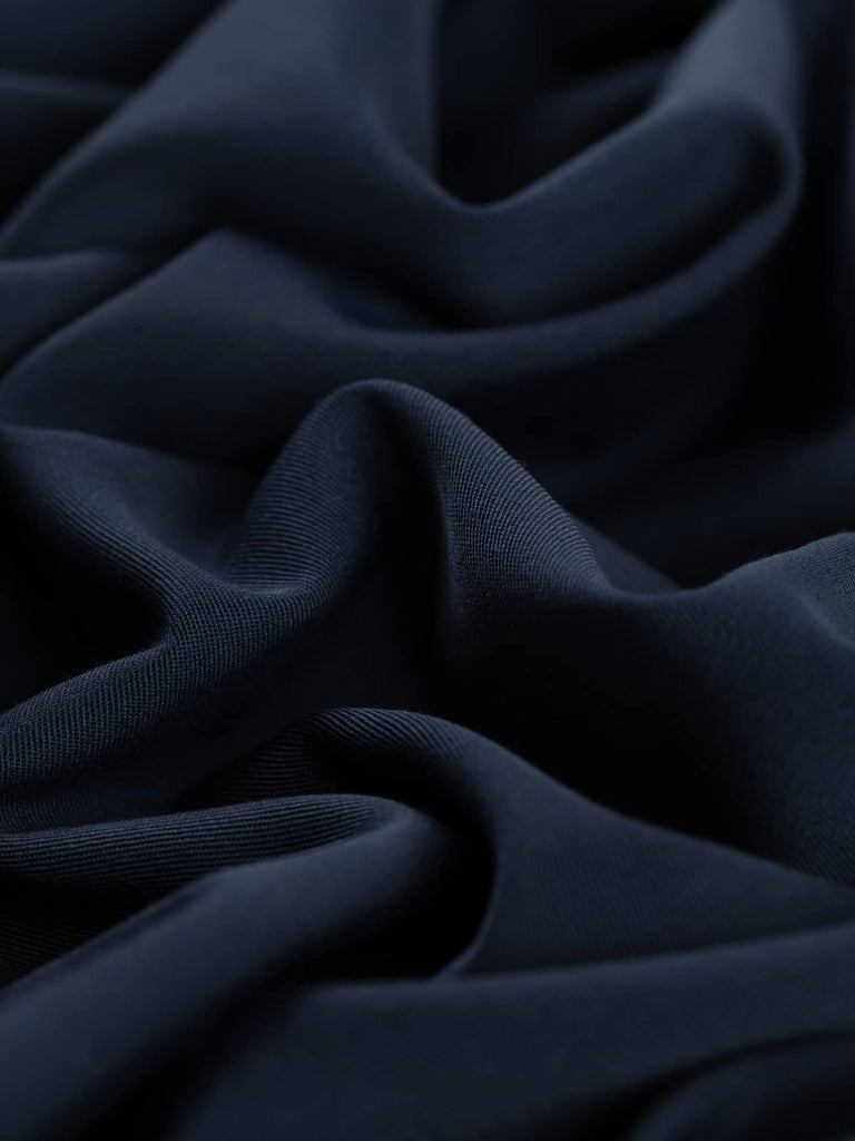 Close-up twist of Sapphire Smoke wool-blend fabric, showing its soft drape, moody navy-grey hue, and fine twill weave with elegant body