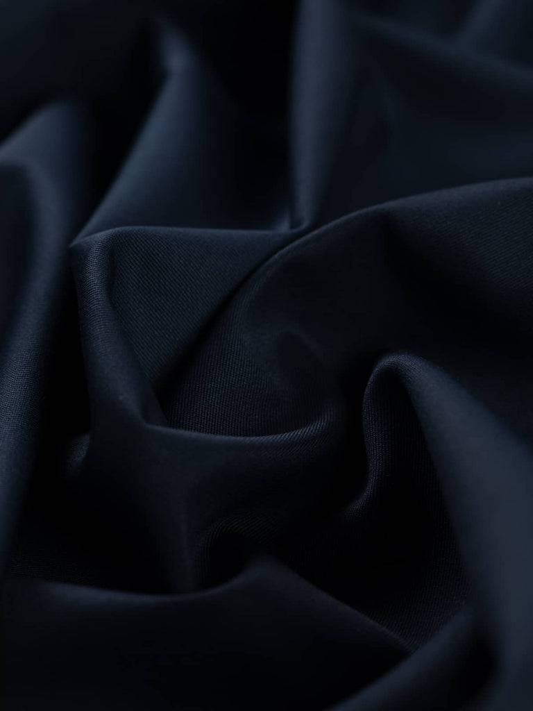 Close-up twist of Twilight Navy wool-blend fabric, showing its soft drape, moody depth of colour, and smooth twill texture with elegant body.