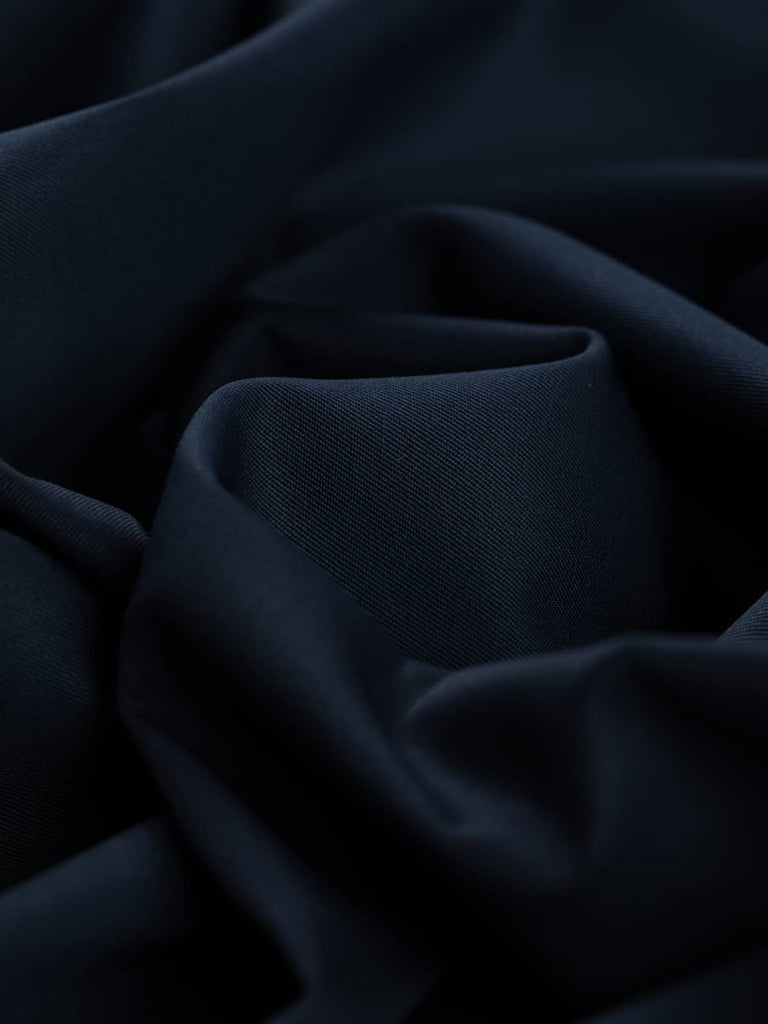Close-up twist of Twilight Navy wool-blend fabric, showing its soft drape, moody depth of colour, and smooth twill texture with elegant body.