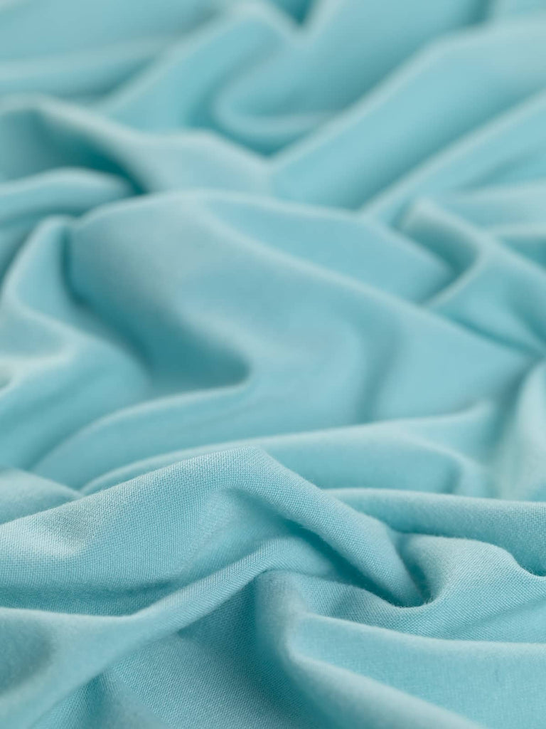 A close-up of the Cosy Soft Single Jersey fabric in Fuzzy Aqua, highlighting its super soft and almost brushed texture. The twisted view emphasizes the fabric's cosy, malleable feel and excellent retentive stretch, perfect for creating comfortable nightwear and loungewear.