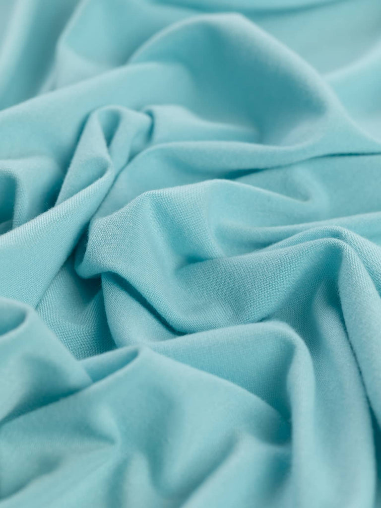 A soft Arctic Blue stretch jersey fabric draped to showcase its fluidity and gentle brushed texture. The cool, pastel aqua hue pairs beautifully with other pastels, and the fabric’s excellent stretch makes it perfect for loungewear and nightwear.