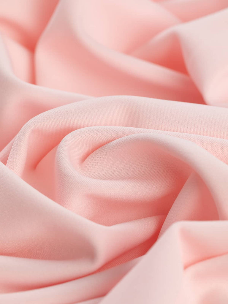 A soft pastel pink scuba-style fabric twisted to showcase its crepe-finished texture and fluid drape. The polyester and elastane blend offers excellent stretch and structure, making it perfect for sculpted sleeves, fitted dresses, and skirts.