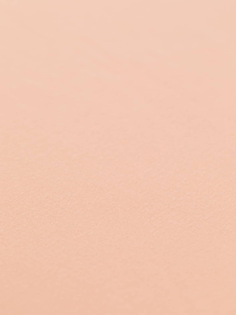 A flat view of the Cosy Soft Single Jersey fabric in Fuzzy Peach, showcasing its solid pastel hue and subtle translucency. The lightweight fabric's soft hand and excellent drape are evident, ideal for creating loose silhouettes with pretty gathers and ruffles.