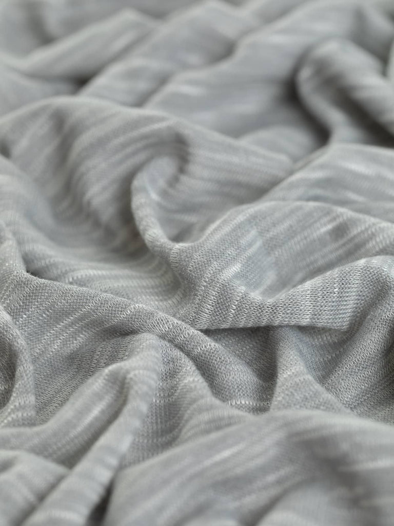 A close-up of the Marled Hacci Viscose Sweater Knit in Smoke, showcasing its fine, light-mid-grey hue with a silvery white marl effect. The twisted fabric highlights its soft, silky, and malleable texture with excellent widthwise stretch, ideal for creating relaxed and chic casual garments.