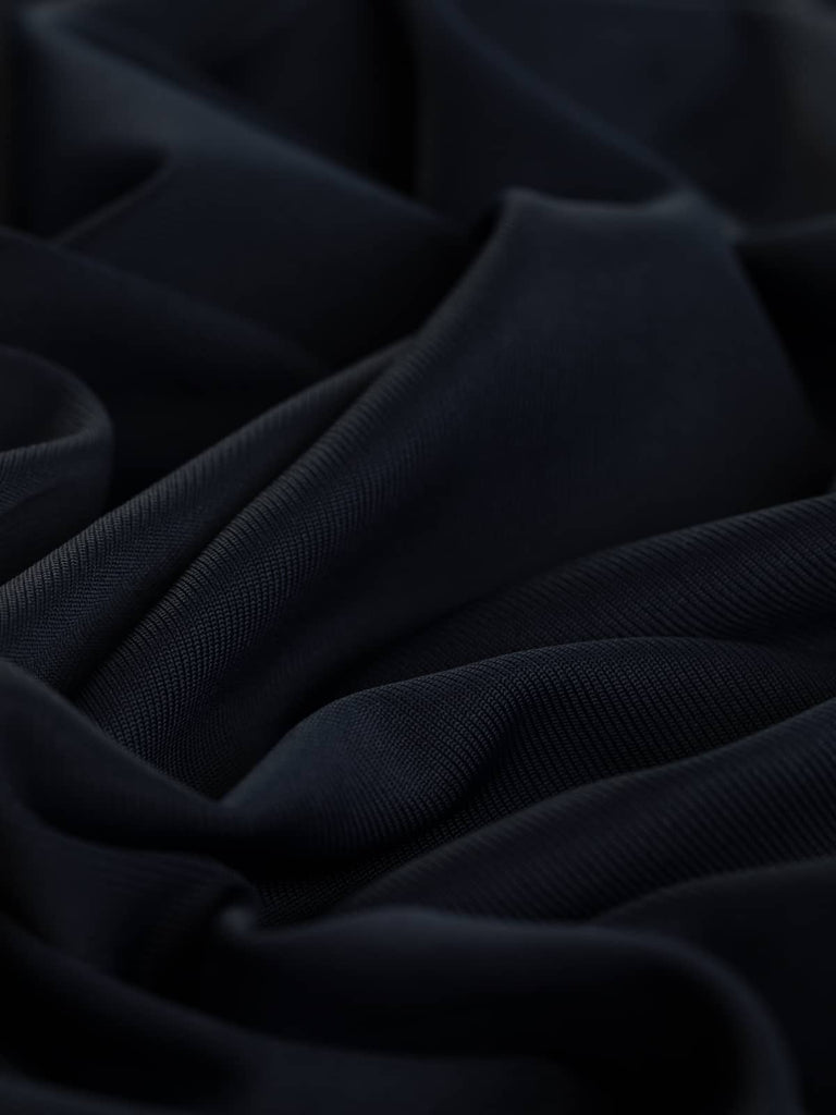 Detailed close-up of Darkest Navy Silken Stretch Rib fabric twisted, highlighting its smooth, silky texture, fine ribbed pattern, and the luxurious stretch and sheen of this versatile polyester, viscose, and Lycra blend.