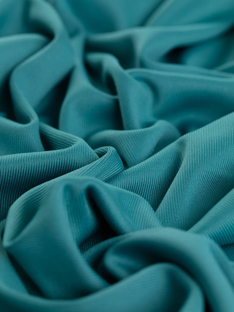 A close-up of the Silken Stretch Rib fabric in Turquoise Jade, showcasing its finely knitted, silky texture with jewel-toned hues. The twist reveals the fabric's soft, cool viscose feel and subtle sheen, highlighting its luxurious quality and stretch.