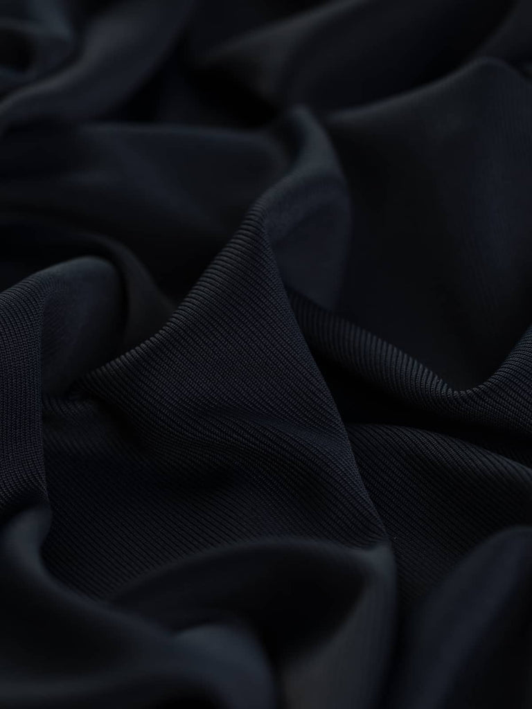 A close-up of the Silken Stretch Rib fabric in Black Navy, highlighting its finely knitted, silky texture with a deep, sophisticated hue. The twist showcases the fabric's soft, cool viscose feel and subtle sheen, emphasizing its luxurious quality and versatile stretch.