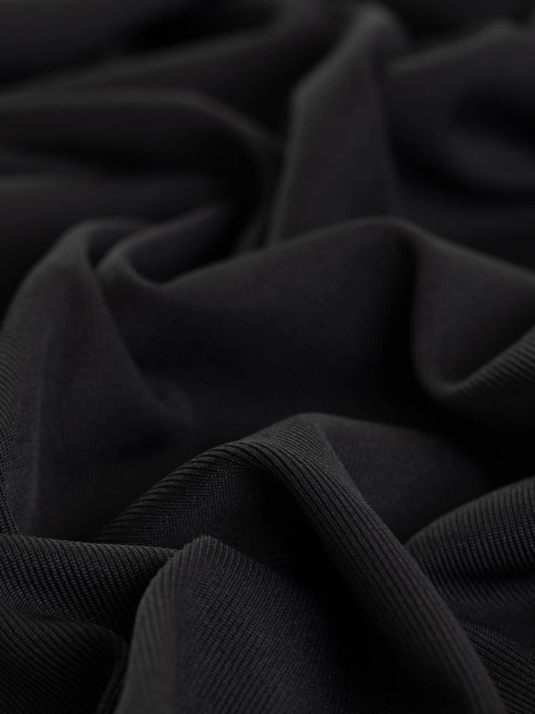 A close-up of the Slinky Stretch Rib fabric in Charcoal Black, showcasing its finely knitted texture with a subtle semi-matte charcoal ash undertone. The twist highlights the fabric's grainy feel and excellent stretch, emphasizing its versatile and practical nature.