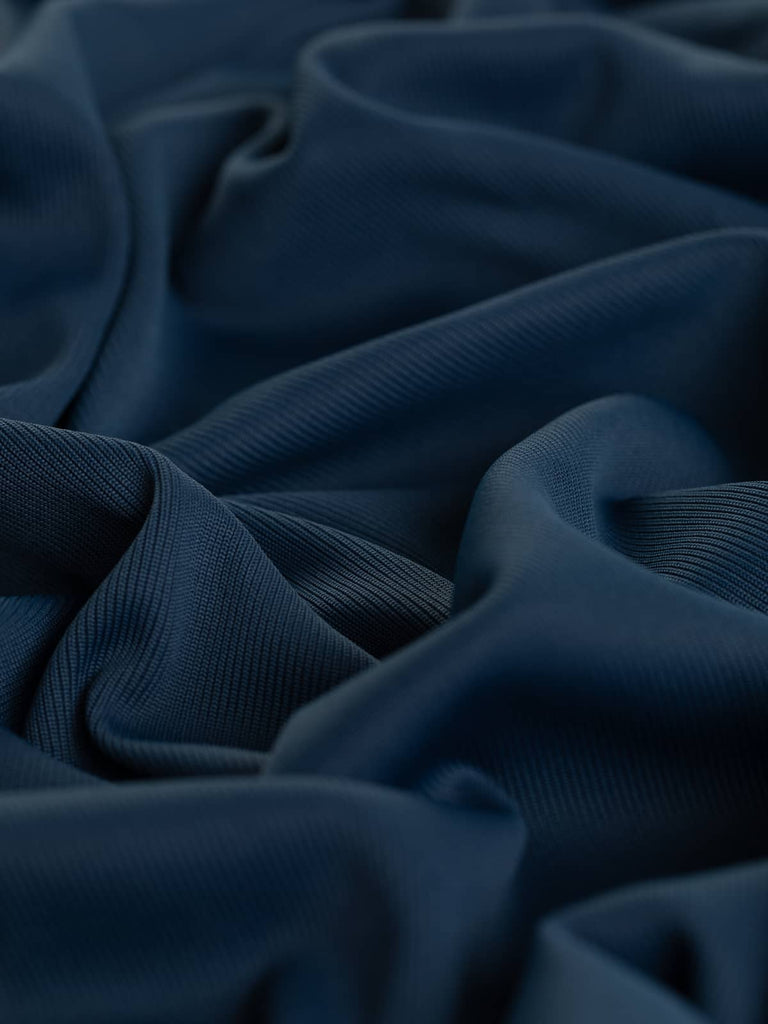 A close-up of the Silken Stretch Rib fabric in French Navy, showcasing its finely knitted texture and rich blue-saturated tone. The twist highlights the fabric's silky, cool viscose feel and excellent stretch, perfect for versatile garment-making.