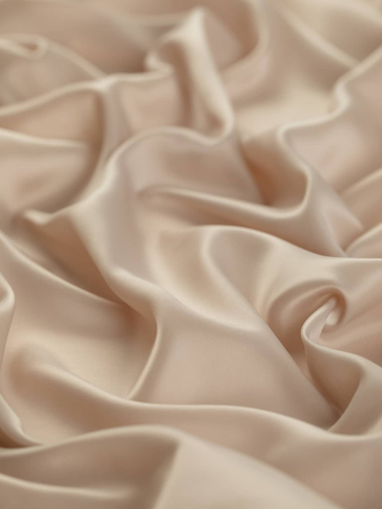 Soft sandy pale beige lining fabric with golden undertones, 142cm wide. This light, 100% polyester woven fabric features a solid flat weave and subtle lustre, ideal for lining jackets, skirts, and dresses, adding a silky, smooth, and drapey feel to corporate and fashion wear.