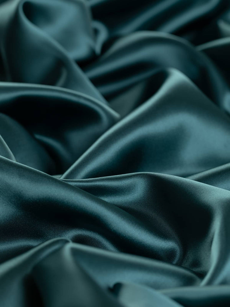 Washed teal blue-green satin lining fabric, 140cm wide, with a silky and lustrous semi-shine. This very light 100% polyester fabric is ideal for adding a smooth, drapey finish to jackets, dresses, and accessories.