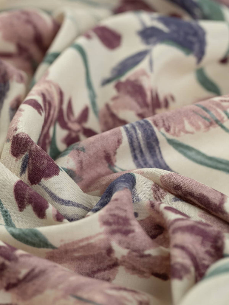 A lightweight linen-viscose challis fabric with a delicate 130 GSM weave, softly twisted to highlight its fluid drape and airy texture. The painterly floral print features elegant irises in vintage-inspired hues of plum, puce pink, navy blue, and muted teal, set against a natural ecru background.