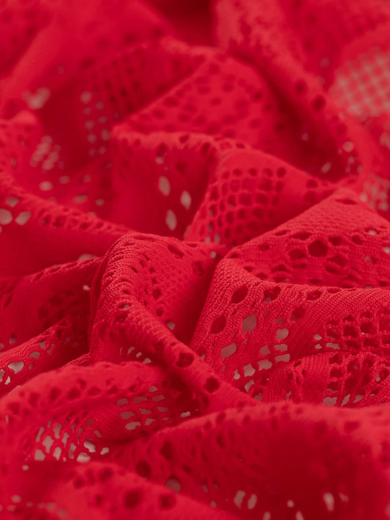 A close-up of the Extra Wide Stretch Mesh Lace - Sundance Red, highlighting the vivid pink-red hues and the intricate lace pattern. The twisted fabric showcases its horizontal stripes, zigzag and diamond chain formations, and the open lace areas, with the largest gaps being 5mm. The 20-30% stretch in both directions is evident, allowing for versatile, fun summer styles.