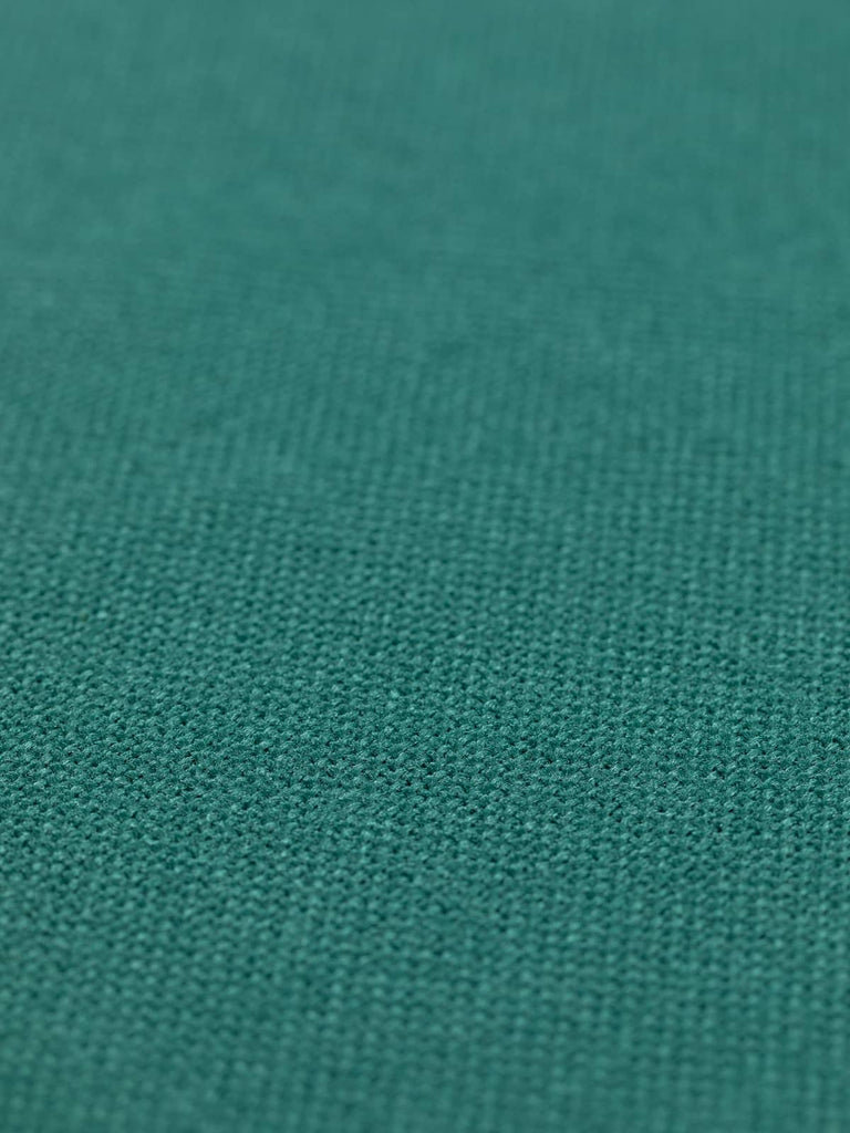 A flat angled view of Antique Verdigris hopsack fabric, accentuating its deep green-blue hue with a grey undertone. The fabric’s solid colour and heavy drape quality create a luxurious and versatile textile, ideal for nature-inspired and stately interior designs.