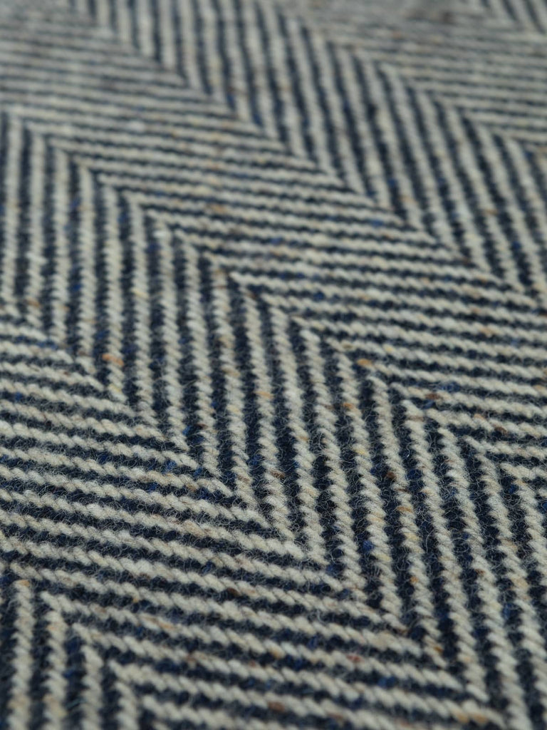 Flat overhead image of Nautical Navy Donegal Herringbone fabric, 154cm wide, displaying bold chevrons and natural flecking in navy and off-white wool.