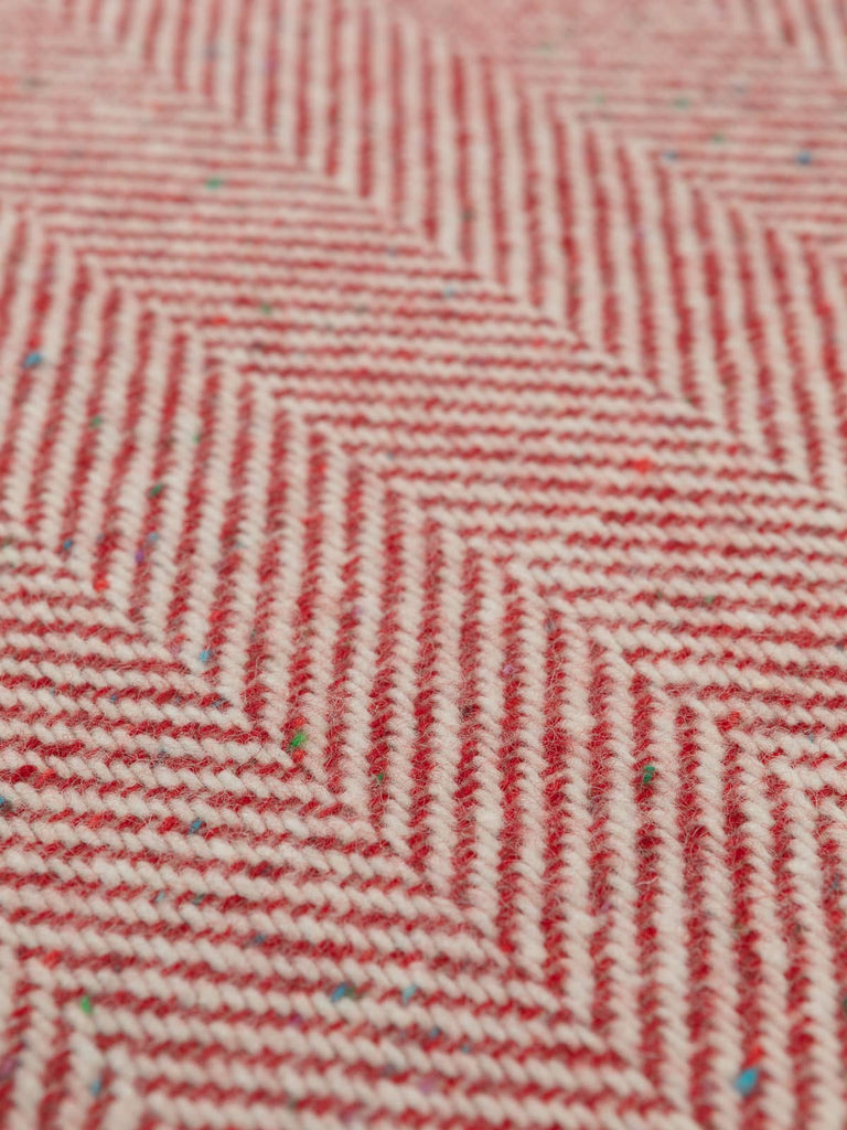 Flat overhead image of Festive Red Donegal Herringbone fabric, 156cm wide, displaying bold chevrons in Scandi red and natural white with colourful neps.