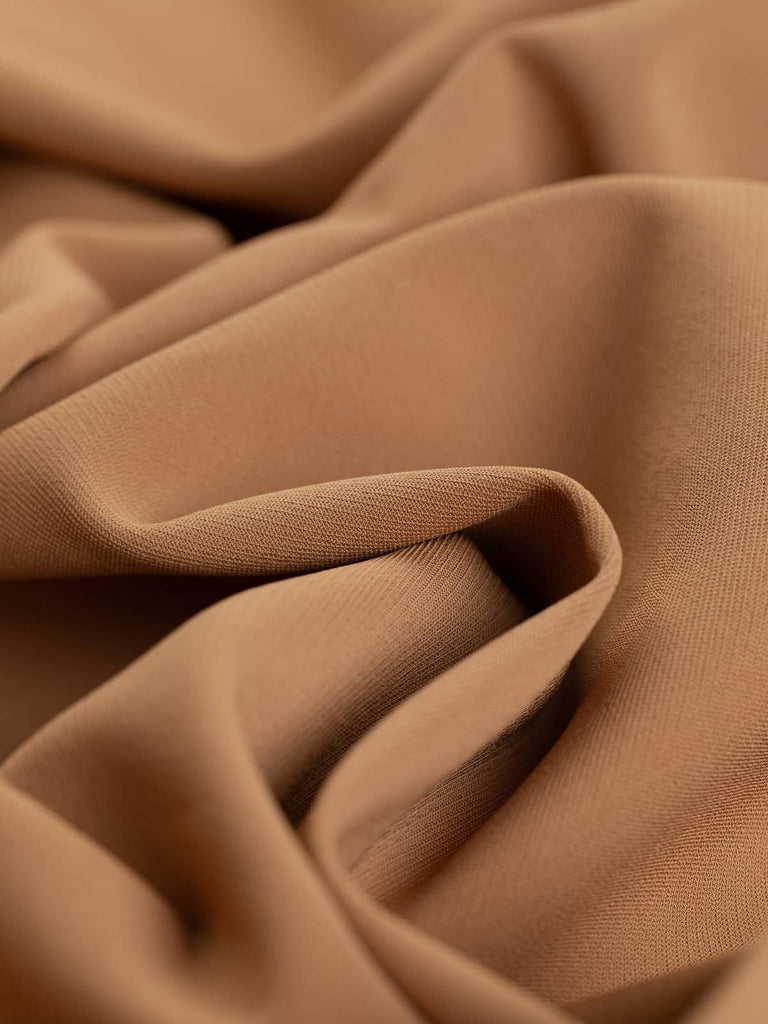 A close-up of the Lycra Viscose Twill - Caramel Gold, showcasing the warm golden caramel beige hue and the twill weave pattern. The twisted fabric highlights its medium weight, heavy drape quality, and slight stretch, making it ideal for classic and stylish apparel. The luxurious, almost crepe-like texture is evident, reflecting its high thread count and designer feel.