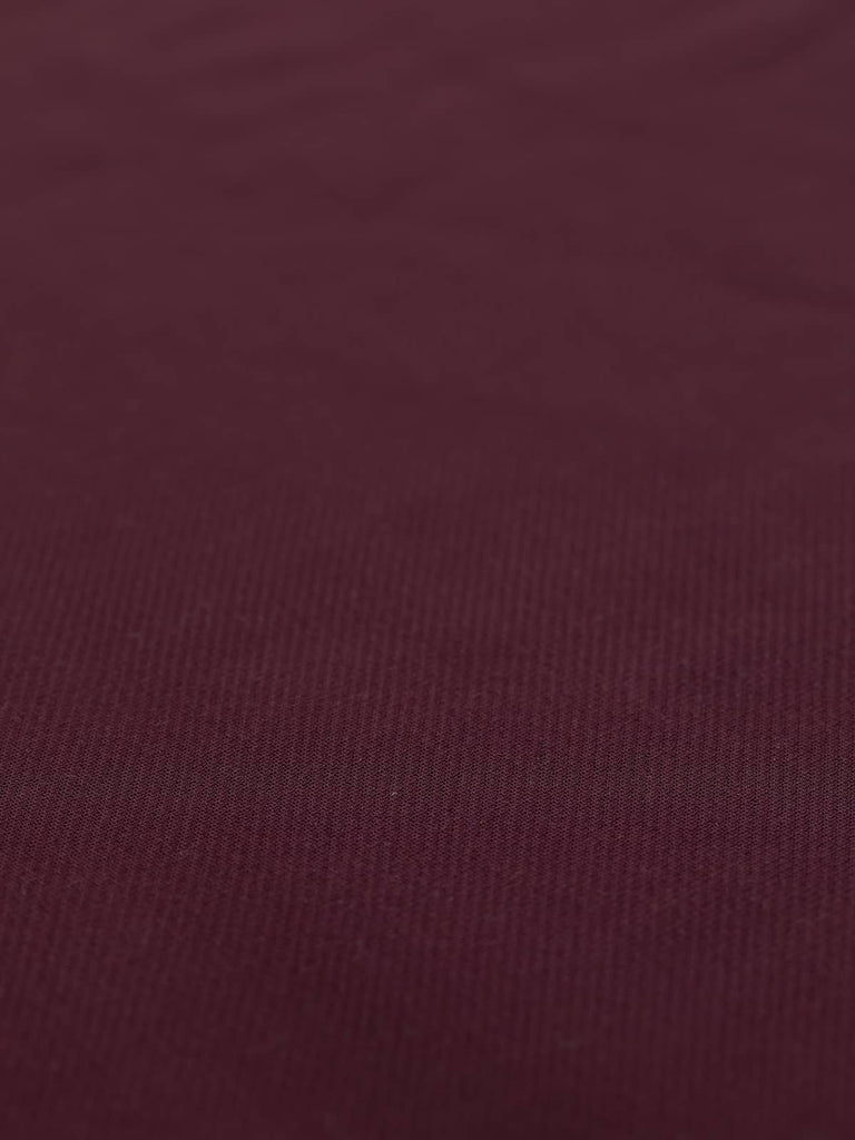 A flat view of the Brushed Back Crepe Twill - Bordeaux, capturing the deep, full-bodied red-purple color that exudes elegance and sophistication. The fine twill weave is clearly visible, emphasizing the fabric's stable hand and medium weight. With a width of 150cm, this fabric is perfect for creating classic and timeless garments such as trench coats, blazers, skirts, and dresses that drape beautifully and offer a luxurious feel against the skin.