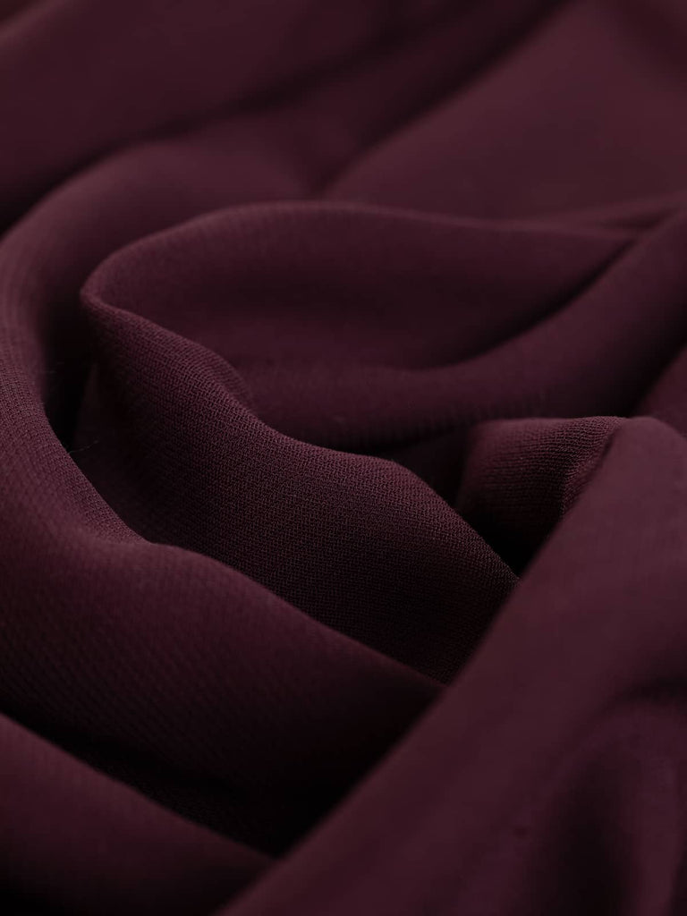 A close-up of the Brushed Back Crepe Twill - Bordeaux, showcasing the rich red-purple hue and the intricate twill weave pattern. The twisted fabric emphasizes the medium weight and the substantial, crepe-like quality, highlighting its stable hand and luxurious texture. The reverse side's charcoal/ash grey hue with its lightly brushed wool flannel feel is also visible, indicating the fabric's versatility and comfort.