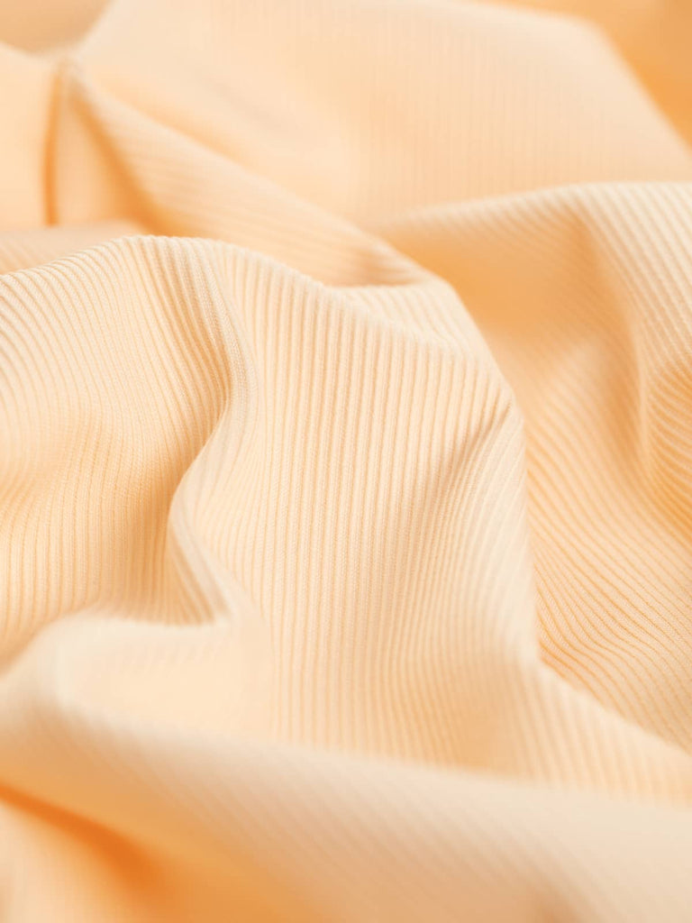 A close-up of the Raised Cotton Twill - Peach Sorbet, showcasing the intricate texture of the finely woven chunky twill. The twisted fabric highlights the medium weight and the lightly textured diagonal lines of the weave, emphasizing the frosted pastel peach hue reminiscent of a refreshing Peach Sorbet. This view demonstrates the fabric's stable and hardwearing nature, akin to medium-weight denim, along with its malleable and drapey quality.