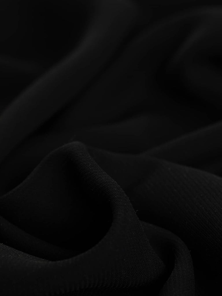 A close-up view of the Brushed Back Crepe Twill - Tuxedo Black, highlighting the intricate fine twill weave and the crepe-like texture. The twisted fabric showcases the medium weight and the luxurious composition of viscose, polyester, and wool. The classic black hue is as timeless and elegant as a black tuxedo or the go-to little black dress. This close-up also reveals the comforting, lightly brushed wool flannel feel of the reverse side, presented in a subtle charcoal/ash grey.