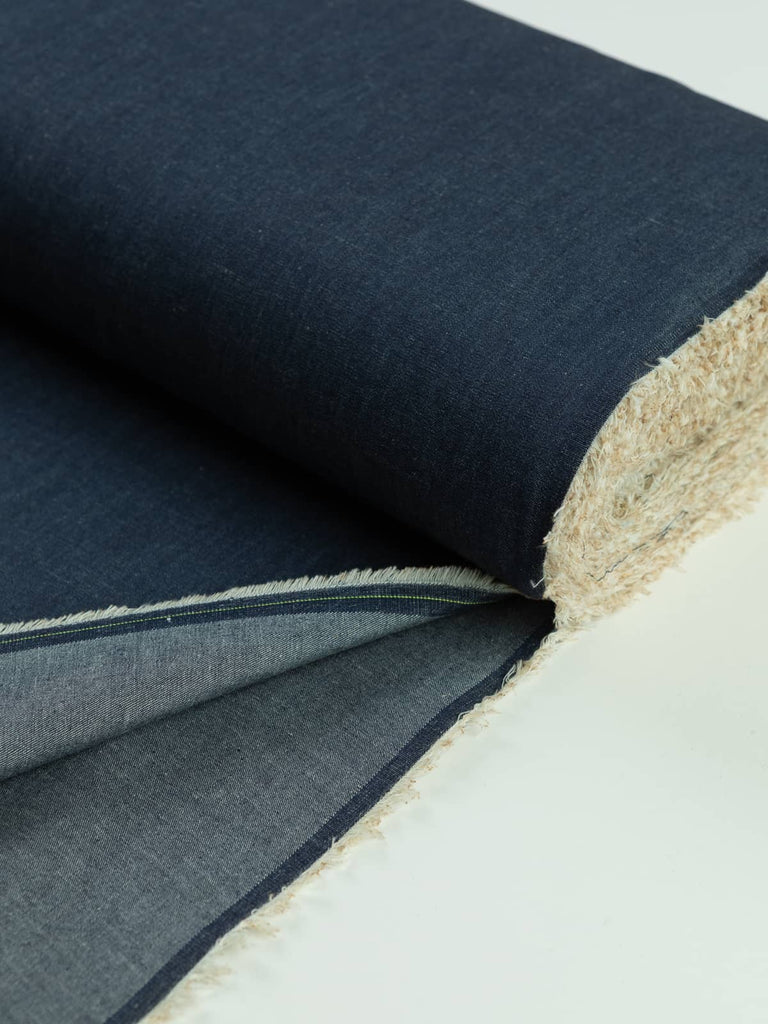 A neatly rolled piece of Dark Indigo chambray denim, highlighting the soft contrast between the deep indigo warp and natural ecru weft. The lightweight fabric is ideal for making summer tops, shirts, and dresses, offering a crisp texture that softens with washing and wear.