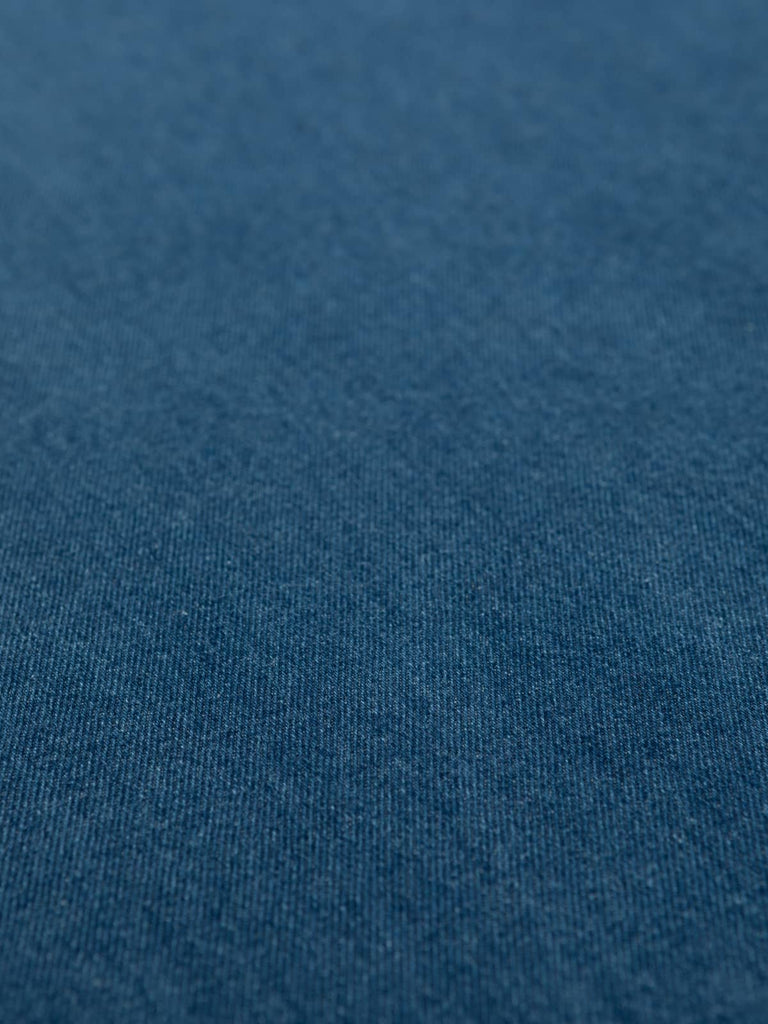 Angled flat view of Workwear Blue Denim fabric, 148cm wide, capturing deep midnight-blue tone, subtle two-tone weave, and durable cotton twill structure with a smooth matte finish.