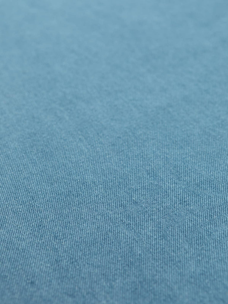 Angled flat view of Summer Skies Cotton Denim, 148cm wide, revealing its light sky-blue hue, smooth structured surface, and gentle two-tone texture from yarn-dyed warp and weft.