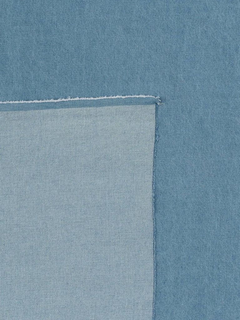 Overhead flat shot of Summer Skies Denim fabric, displaying its pale blue tone inspired by sun-washed vintage workwear, balanced by the creamy natural reverse and defined twill grain.