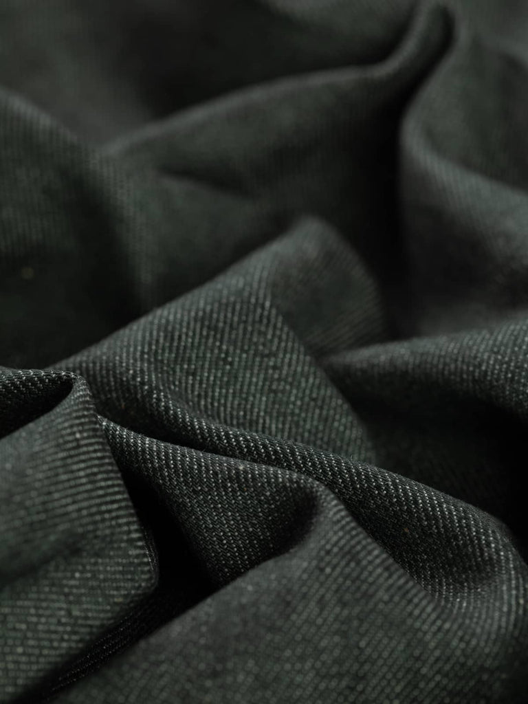 A close-up of Charcoal Denim fabric twisted at an angle, showcasing its rich washed black hue with subtle natural white weft threads. The soft yet structured texture and classic diagonal twill weave are visible, highlighting the fabric’s durability and versatility.