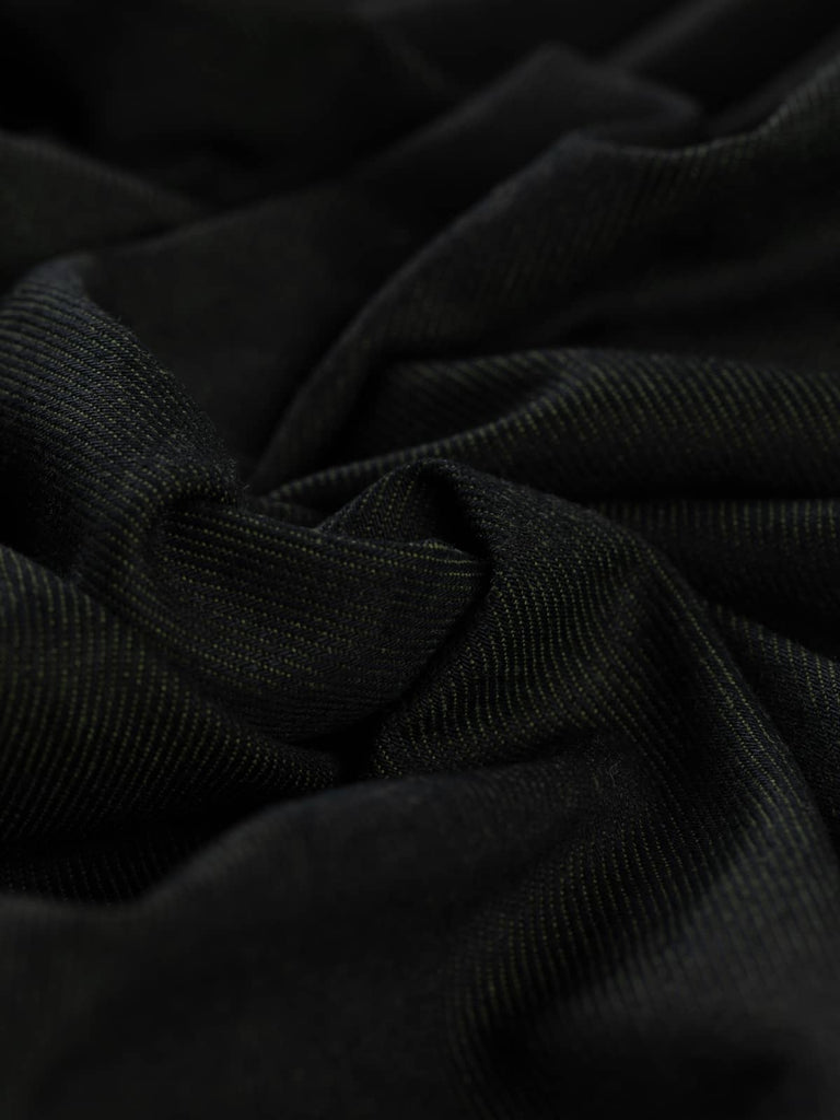 A close-up of Khaki Shot Denim fabric twisted at an angle, showcasing its deep green-black hue with subtle khaki undertones. The soft yet structured cotton material and diagonal twill weave are clearly visible, emphasizing its durability and versatility.