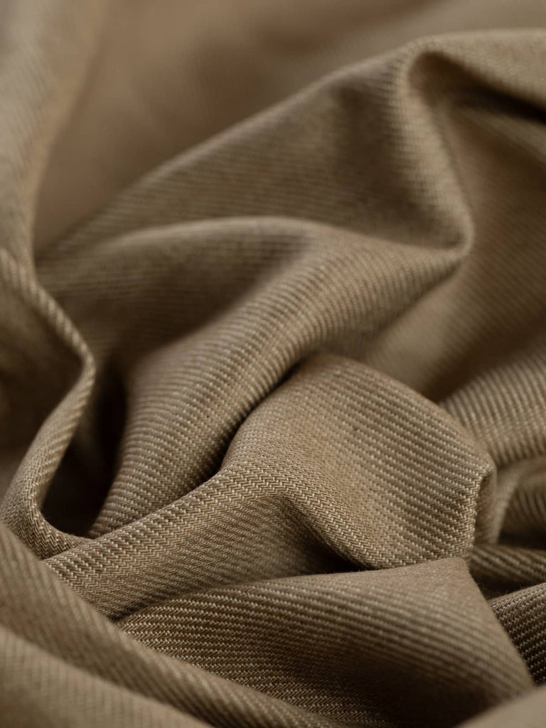  A close-up of Sand Denim fabric twisted to reveal its soft, warm beige hue and classic workwear twill texture. The cotton yarns, with a natural feel, blend seamlessly, creating a durable yet comfortable fabric that has a refined and versatile look.