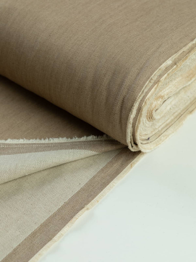 A neatly rolled piece of Sand Denim fabric showcasing its light, sandy beige color and stable, semi-structured nature. The diagonal ridges of the twill weave are clearly visible, adding depth and durability to this timeless, multi-purpose textile.