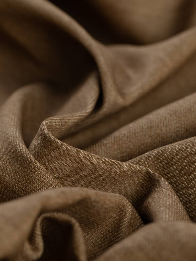 A close-up of Tawny Denim fabric twisted to highlight its warm beige hue with soft golden-brown cotton yarns creating a subtle, earthy, workwear-inspired aesthetic. The fabric’s diagonal twill weave showcases its durable and stable structure while offering a soft, comfortable feel.