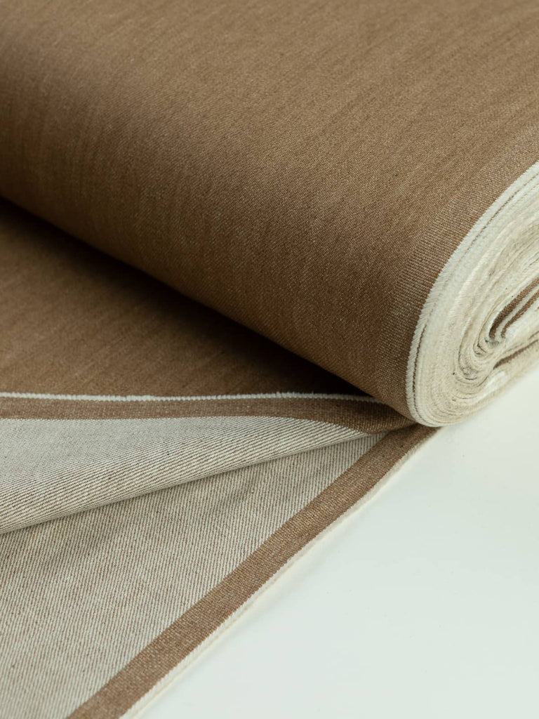 A neatly rolled piece of Tawny Denim fabric in a golden beige tone, showcasing the close, hard-wearing weave of this medium-weight denim. The natural cotton yarns in the warp and weft create a versatile, classic look with durability that softens over time with wear.