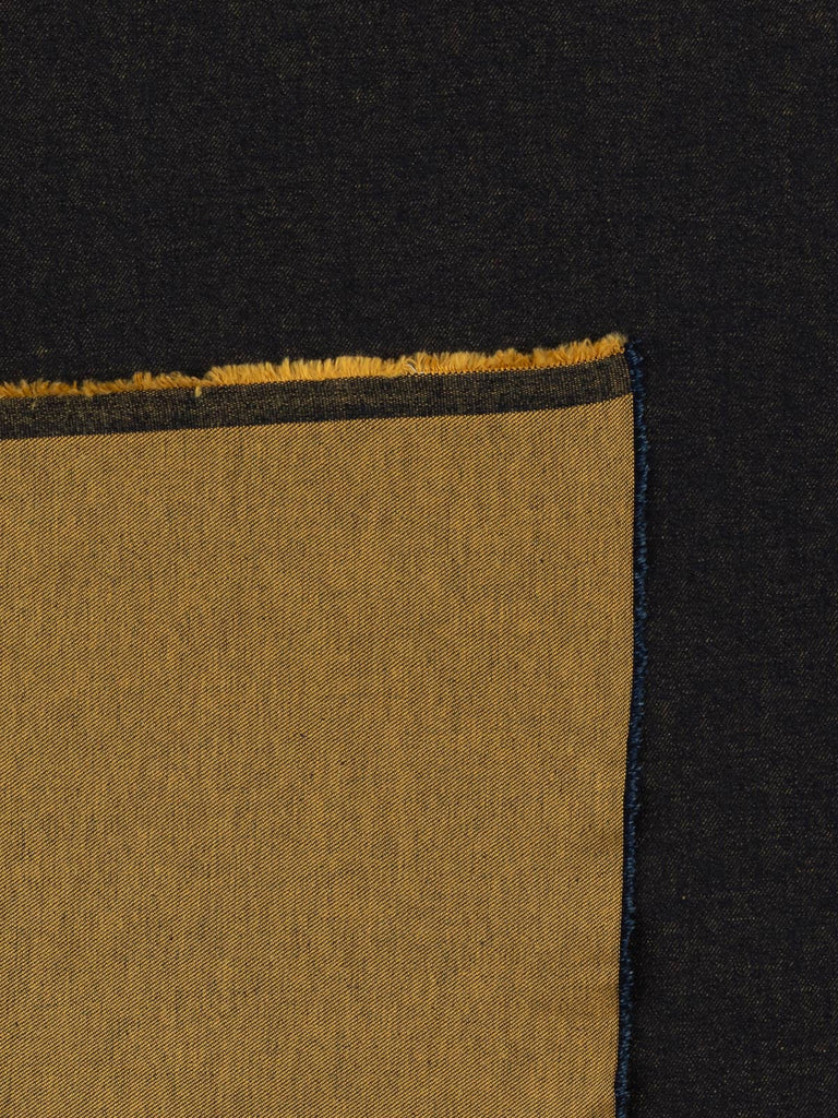 Overhead flat shot of Mustard Shot Denim fabric, capturing the rich interplay between dark navy warp and golden mustard weft, producing a sophisticated shot-effect surface with classic twill definition.