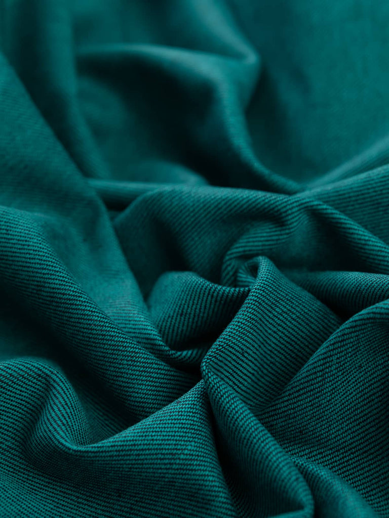 Twist of Teal Shot 100% Cotton Denim, 370gsm, showing deep indigo-blue face woven with teal-green weft yarns, producing a reversible two-tone surface with distinctive twill movement and defined structure.